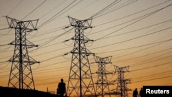 FILE - Locals walk past electricity pylons during frequent power outages from South African utility Eskom, caused by its aging coal-fired plants, in Soweto, South Africa. Taken July 3, 2022.