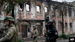 Ukrainian servicemen walk past heavily damaged building in the recaptured area in Izium, Sept. 14, 2022.
