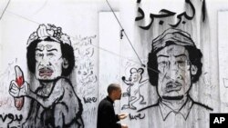 A man passes graffiti caricatures related to Moammar Gadhafi and Brega, during a funeral in Benghazi, April 19, 2011