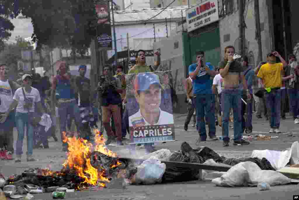 Demonstrators, one holding a poster of opposition presidential candidate Henrique Capriles, confront riot police from behind a burning barricade in the Altamira neighborhood in Caracas, April 15, 2013.