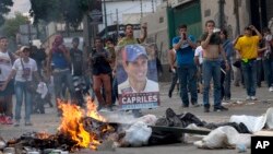 Para pendukung pemimpin oposisi Henrique Capriles, berlindung di balik barikade ban yang dibakar di jalanan saat berhadapan dengan polisi anti huru-hara di wilayah Altamira, Caracas (15/4).