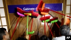 Ministerial staff use brooms to scrub the office door of the Transparency Minister Fabiano Silveira demanding his resignation, in Brasilia, Brazil, Monday, May 30, 2016. A recording TV Globo broadcast late Sunday shows Silveira criticizing Operation Car Wash, a wide-ranging corruption probe of the state oil company Petrobras that has implicated numerous leading Brazilian politicians and businessmen. Protesters in Brazil use brooms as a representation to sweep away corruption. (AP Photo/Eraldo Peres)