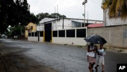 FILE - People walk near a factory where Aragua State police officers killed four men execution-style in Maracay, Venezuela, Aug. 20, 2015. 