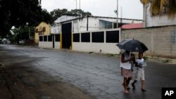 People walk near a factory where Aragua State police officers killed four men execution-style in Maracay, Venezuela, Aug. 20, 2015. 