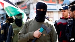 Masked member of Hamas holds an axe on his chest as others wave their national flags during a protest against the Mideast plan announced by U.S. President Donald Trump, after the Friday prayer at the main road in Gaza City, Friday, Jan. 31, 2020.