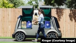 A woman walks in front of an unmanned delivery vehicle known as the R1 in this handout photo provided by Kroger.
