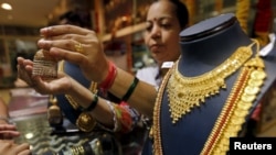 FILE - A saleswoman shows a gold earring to customers at a showroom in Mumbai, India.