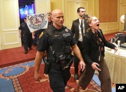 About 25 protesters are escorted by police after interrupting a energy summit where U.S. Energy Secretary Rick Perry spoke, May 30, 2019, in Salt Lake City. Perry says the Trump administration is committed to making fossil fuels cleaner rather than imposing "draconian" regulations on oil, gas and coal.