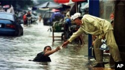 A Cambodian amputee beggar is given money by a passerby while wading in the street flood in Phnom Penh.