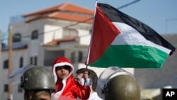 FILE - A Palestinian child dressed as Santa Claus holds a Palestinian flag while standing in front of Israeli Border Police during a demonstration in Al-Masara, near Bethlehem, Dec. 20, 2013 
