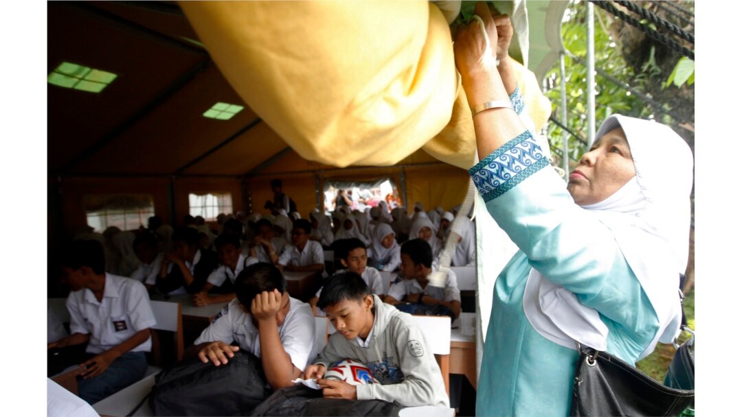 Seorang guru menggulung sebagian tenda UNICEF sebagai siswa belajar di sekolah mereka setelah dibuka kembali untuk kelas setelah gempa bumi Padang, Sumatera Barat, 5 Oktober 2009. (Foto: Reuters/Dadang Tri)