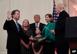 Retired Justice Anthony Kennedy, right, ceremonially swears-in Supreme Court Justice Brett Kavanaugh, as President Donald Trump looks on, in the East Room of the White House in Washington, Oct. 8, 2018. Ashley Kavanaugh holds the Bible and daughters Margaret, left, and Liza, look on.