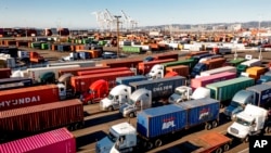 FILE - Trucks line up to enter a Port of Oakland shipping terminal, Nov. 10, 2021, in Oakland, Calif. The federal government is moving forward with a plan to let teenagers drive big rigs from state to state in a test program.