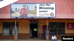 A woman sits beneath a billboard for the National Union of Mineworkers in South Africa's North West province on Oct. 13, 2012.