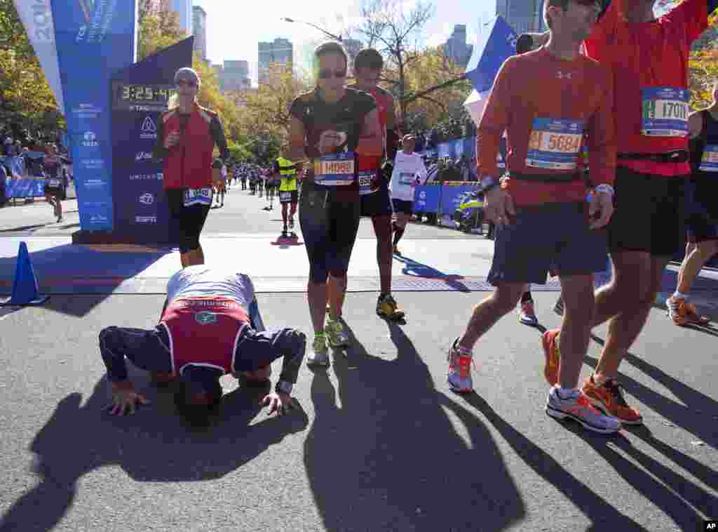 A runner kneels on the pavement as participants stream across the finish line during the New York City Marathon in New York, Nov. 2, 2014.