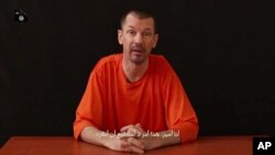 FILE - Captive British journalist John Cantlie speaks into the camera on the first of what he says will be a series of lecture-like "programs" in which he says he will reveal "the truth" about the Islamic State group.