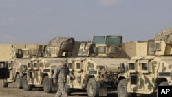 U.S. army soldiers walk past military armored vehicles ready to be shipped out of Iraq at Camp Victory Baghdad, Iraq, November 7, 2011.