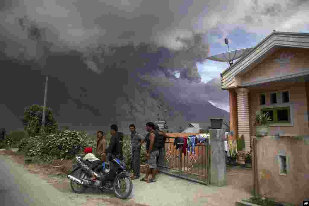 Villagers gather in front of a house as they watch Mount Sinabung releasing a pyroclastic flow during its eruption in Karo, North Sumatra, Indonesia.