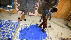 Senegalese artist Omar Ba walks over a large canvas while wearing ink-dipped sandles at his studio in Bambilor, Senegal on March 12, 2021.