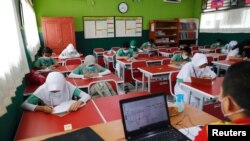 Siswa sekolah dasar mengenakan masker dan duduk sesuai aturan untuk menjaga jarak sosial, kembali belajar di kelas mereka, saat sekolah dibuka kembali di tengah pandemi COVID-19 di Bekasi, 24 Maret 2021. (REUTERS / Willy Kurniawan)
