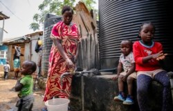In this April 10, 2020, photo, Judith Andeka a widow and mother of five, fetches water with a bucket in the Kibera slum, or informal settlement, of Nairobi, Kenya. (AP Photo/Brian Inganga)