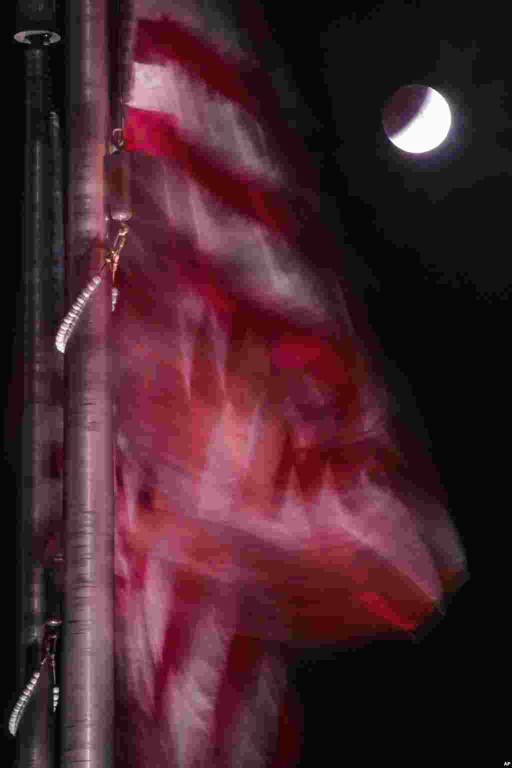 American flags blow in the breeze as a lunar eclipse projects the Earth's shadow onto the moon, near the Washington Monument in Washington, DC, Oct. 8, 2014.