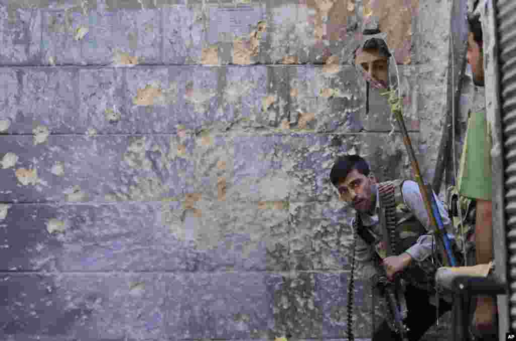 A Free Syrian Army soldier, right, looks through a mirror which helps him see Syrian troops from the other side, as he takes his position with his comrade during fighting, in Aleppo, Syria, Sept. 24, 2012.