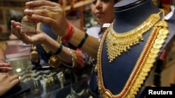 A saleswoman shows a gold earring to customers at a jewelry showroom in Mumbai, India, July 21, 2015. 