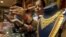 FILE - A saleswoman shows a gold earring to customers at a showroom in Mumbai, India.
