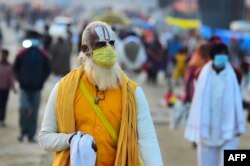 Seorang Sadhu mengenakan masker sberjalan di Sangam, pertemuan Sungai Gangga, Yamuna, dan Sungai Saraswati yang mistis selama festival Magh Mela di Allahabad pada 25 Januari 2022. (Foto: AFP/Sanjay Kanojia)