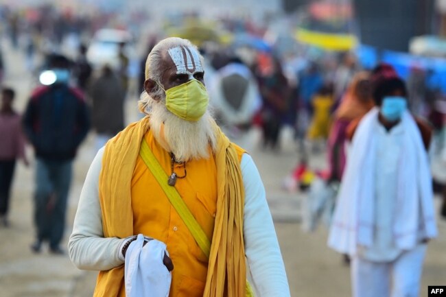 Seorang Sadhu mengenakan masker sberjalan di Sangam, pertemuan Sungai Gangga, Yamuna, dan Sungai Saraswati yang mistis selama festival Magh Mela di Allahabad pada 25 Januari 2022. (Foto: AFP/Sanjay Kanojia)
