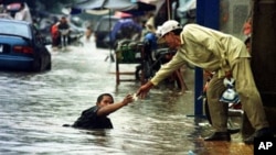 A Cambodian amputee beggar is given money by a passerby while wading in the street flood in Phnom Penh.