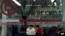 Dua pria membaca koran di depan kantor cabang Bank of China, di Guangzhou, selatan provinsi Guangdong (Foto: dok).