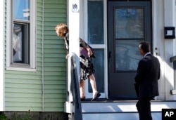 Carrie Sideris, of Newton, Mass., talks to a resident through a window accompanied by her husband, Dan Sideris, as they return to door-to-door visits as Jehovah's Witnesses, Sept. 1, 2022, in Boston. Evangelizers are being advised to be mindful that lives and attitudes have changed in recent years.