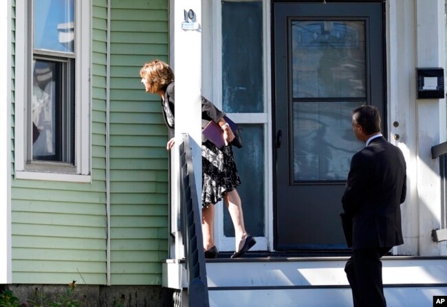 Carrie Sideris, of Newton, Mass., talks to a resident through a window accompanied by her husband, Dan Sideris, as they return to door-to-door visits as Jehovah's Witnesses, Sept. 1, 2022, in Boston. Evangelizers are being advised to be mindful that lives and attitudes have changed in recent years.