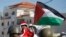 FILE - A Palestinian child dressed as Santa Claus holds a Palestinian flag while standing in front of Israeli Border Police during a demonstration in Al-Masara, near Bethlehem, Dec. 20, 2013 