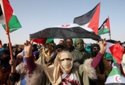 Sahrawi people carry flags as they gather to watch a parade at the Awserd refugee camp in Tindouf, Algeria, Feb. 27, 2021.