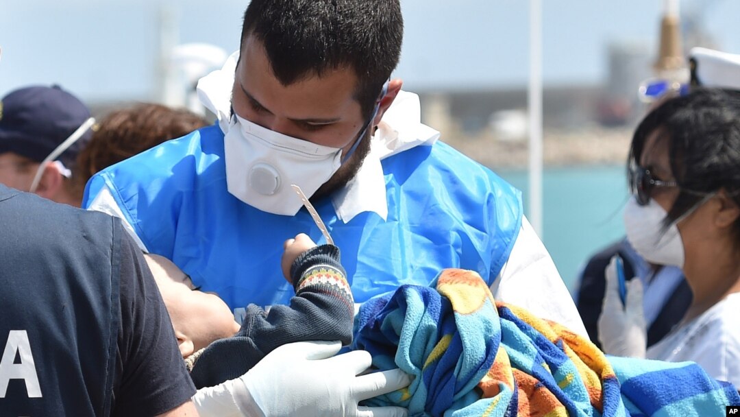 Seorang petugas paramedik memegang bayi yang dibungkus selimut di tengah kedatangan migran di pelabuhan Pozzallo dekat Ragusa, Sisilia di Italia (19/5). (AP/Carmelo Imbesi)