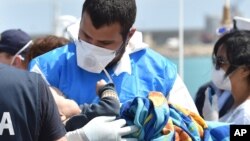 Seorang petugas paramedik memegang bayi yang dibungkus selimut di tengah kedatangan migran di pelabuhan Pozzallo dekat Ragusa, Sisilia di Italia (19/5). (AP/Carmelo Imbesi)