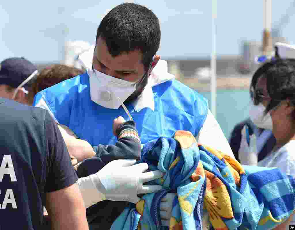 A paramedic holds a baby wrapped in a blanket as migrants arrive at Pozzallo&#39;s harbor near Ragusa, Sicily, Italy.