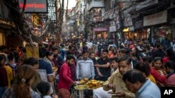 People eat street food as shoppers crowd a market in New Delhi, India, Nov. 12, 2022.