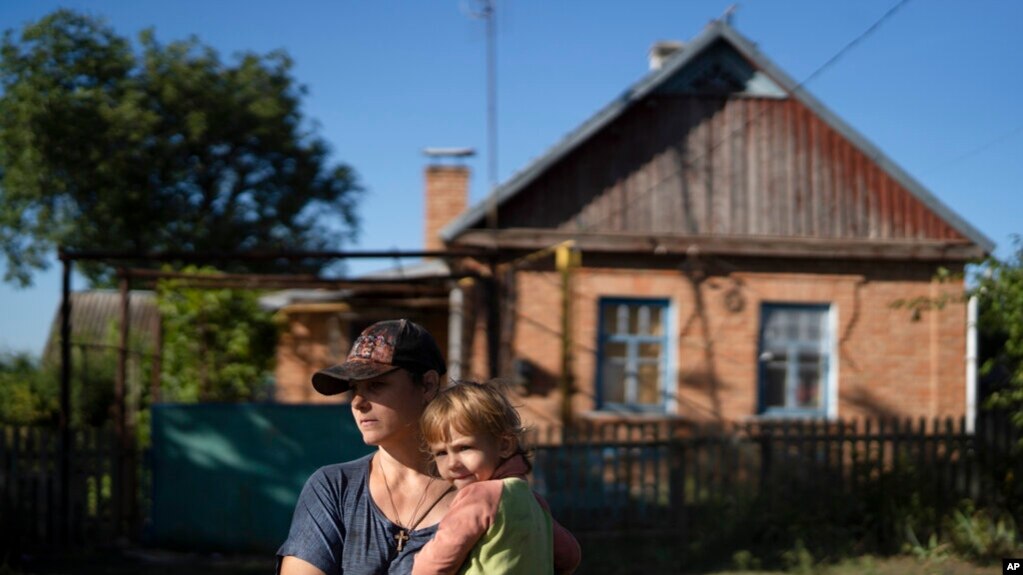 2022年9月2日，乌克兰，娜塔莉亚·斯托科兹抱着她3岁的女儿维罗妮卡站在距扎波罗热核电站约20公里的佐里亚村的房子前。(photo:VOA)
