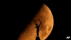 A statue of a Kansa warrior titled &quot;Ad Astra,&quot; atop the Kansas Statehouse is silhouetted against the setting moon in Topeka, Kansas.