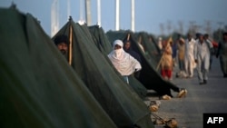 Internally displaced flood-affected people gather outside their tents at a makeshift camp alongside flood waters after heavy monsoon rains in Sukkur, Sindh province, Sept. 5, 2022.