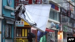 A man walks under the wreckage of a damaged signboard in a shopping area of Changwon on Sept. 6, 2022, as Typhoon Hinnamnor hit South Korea's southern provinces. (Yonhap via AFP)