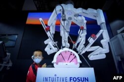 北京举行的2022世界机器人大会上一名儿童在注视一个可以进行外科手术的机械手。（2022年8月18日）