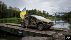 Paracaidistas ucranianos con la bandera ucraniana conducen en el puente de pontones que cruza el río Siverskyi-Donets en el área recientemente recuperada de Izium, Ucrania, el 14 de septiembre de 2022.