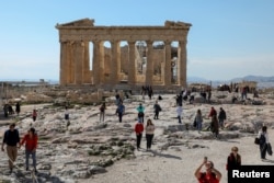 FILE - People visit the ancient Parthenon Temple atop the Acropolis hill archaeological site in Athens, Greece, Feb. 26, 2022.