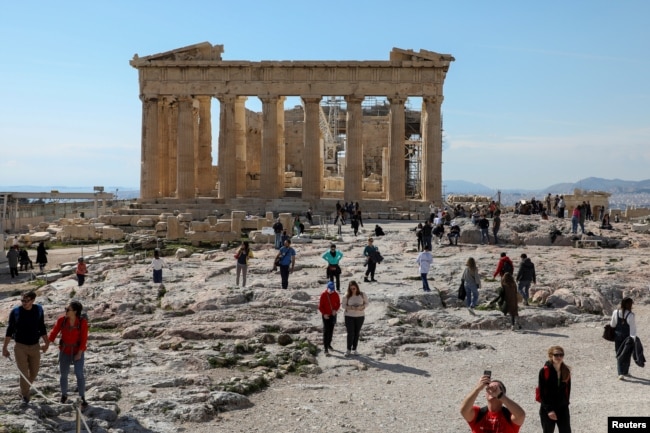 FILE - People visit the ancient Parthenon Temple atop the Acropolis hill archaeological site in Athens, Greece, Feb. 26, 2022.