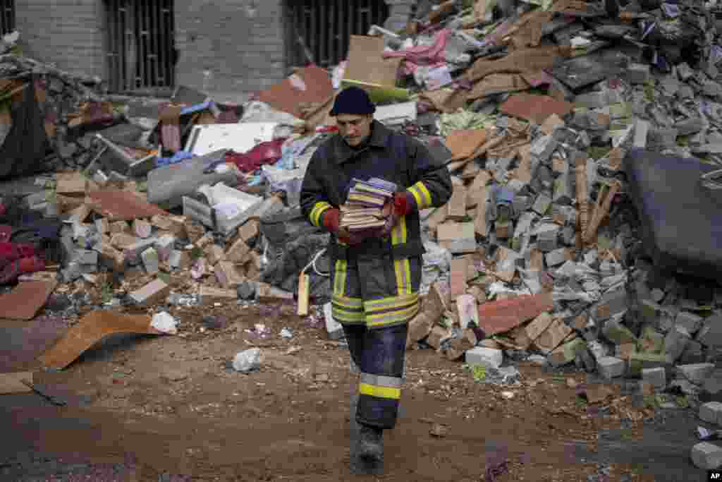 Un bombero lleva unos libros lejos de los restos de una casa tras un ataque ruso en Cherníhiv, Ucrania, el viernes 22 de abril de 2022. (AP Foto/Emilio Morenatti)